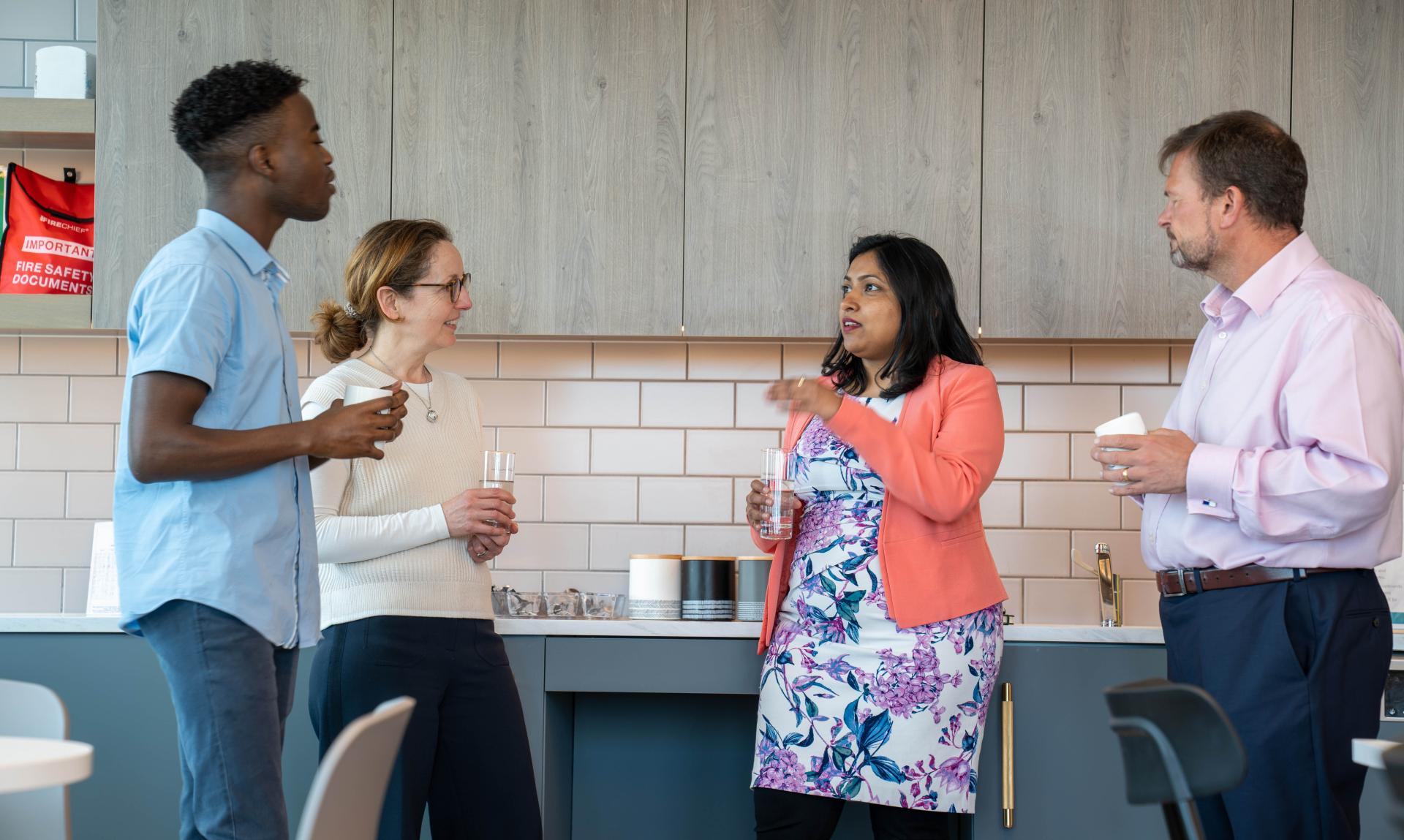 A group of four people talking and in a kitchenette.